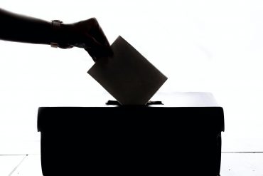 Silhouette of voter placing ballot in ballot box.